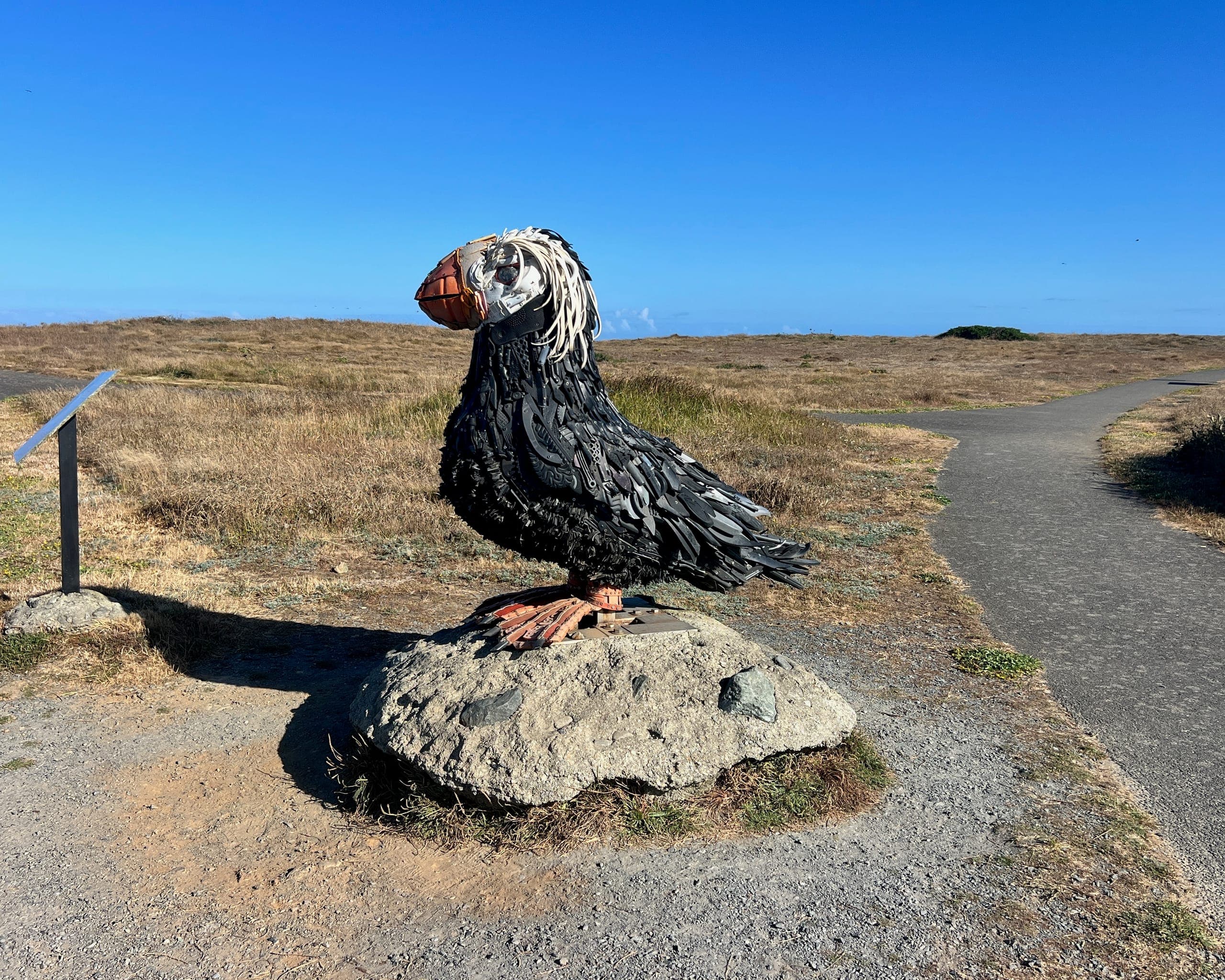 A statue of a puffin perched on a rock situated on a cliff overlooking the ocean.