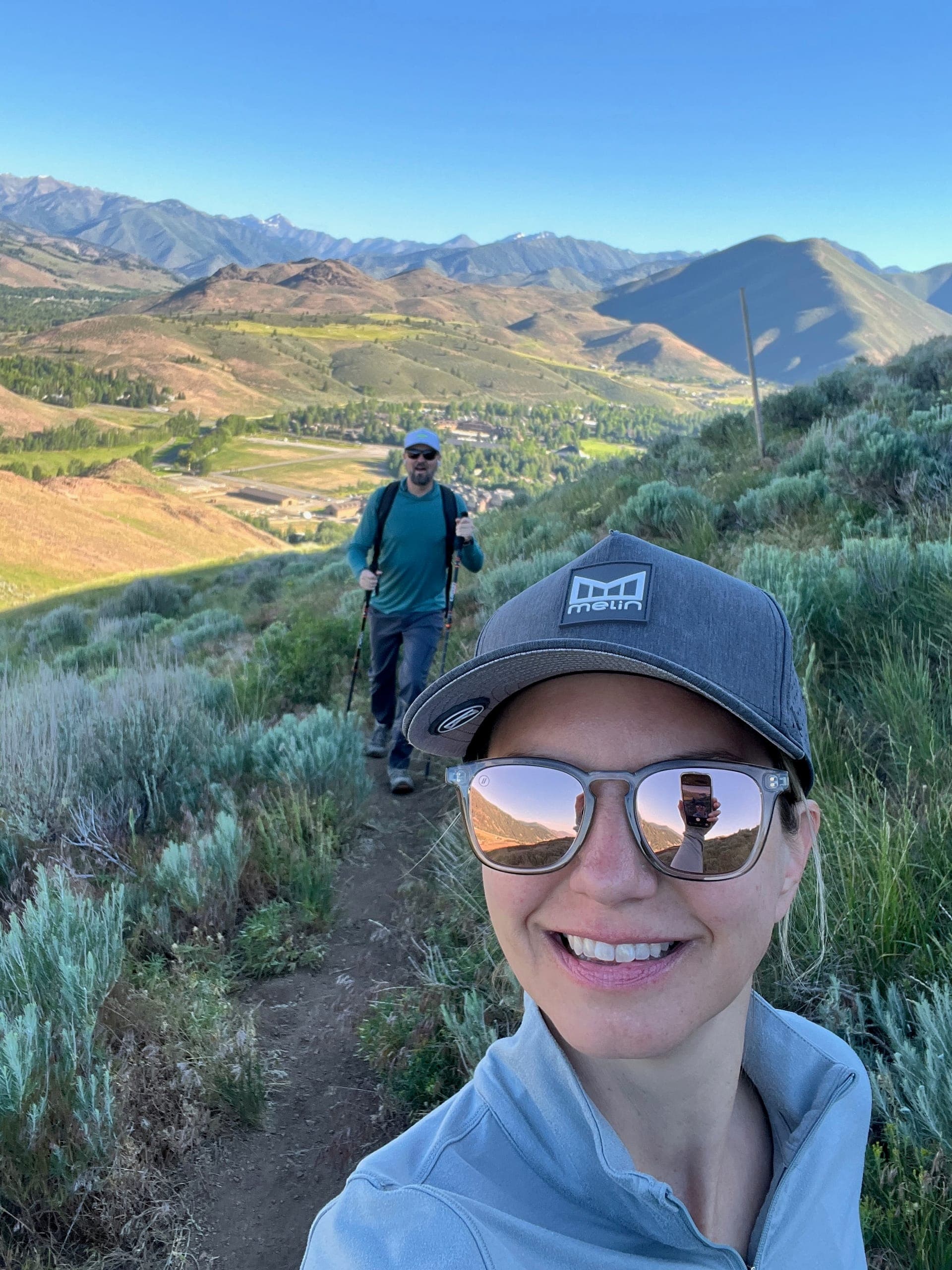 Sarah taking a selfie with Erik hiking behind her.