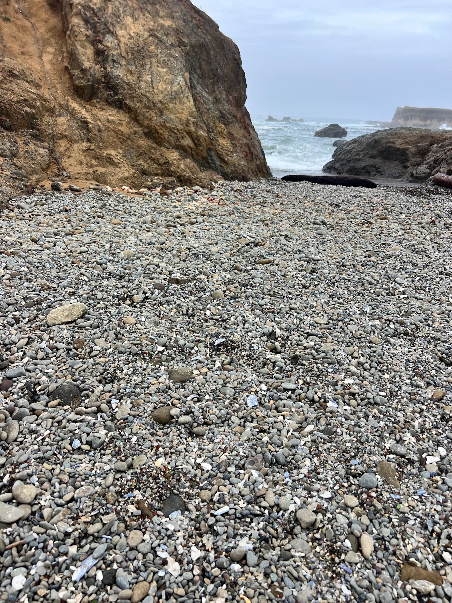 Rocks and small rounded pieces of glass on the beach with rock outcroppings in the background.