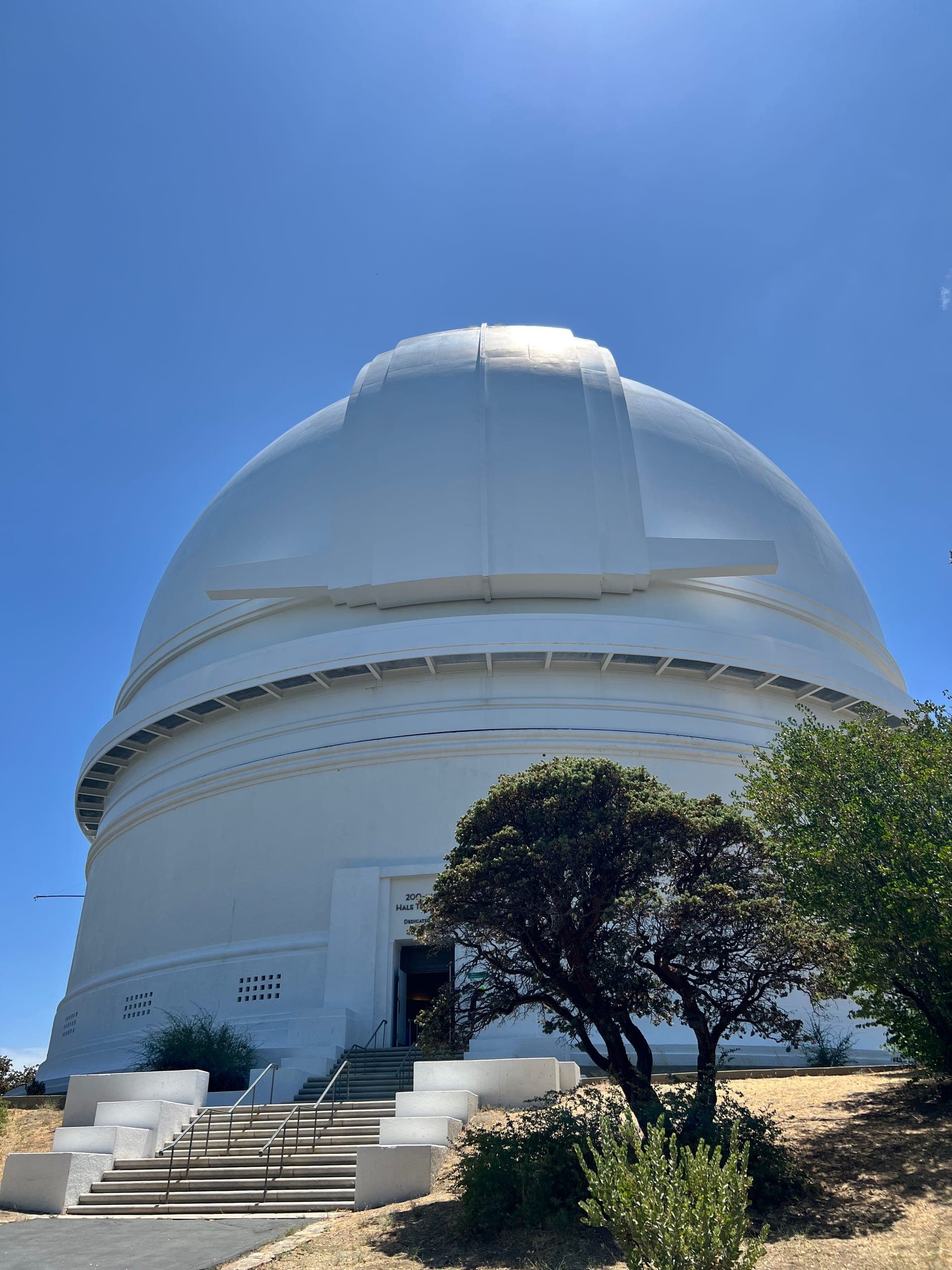 The white dome of the exterior of the Palomar Observatory against a blue sky.