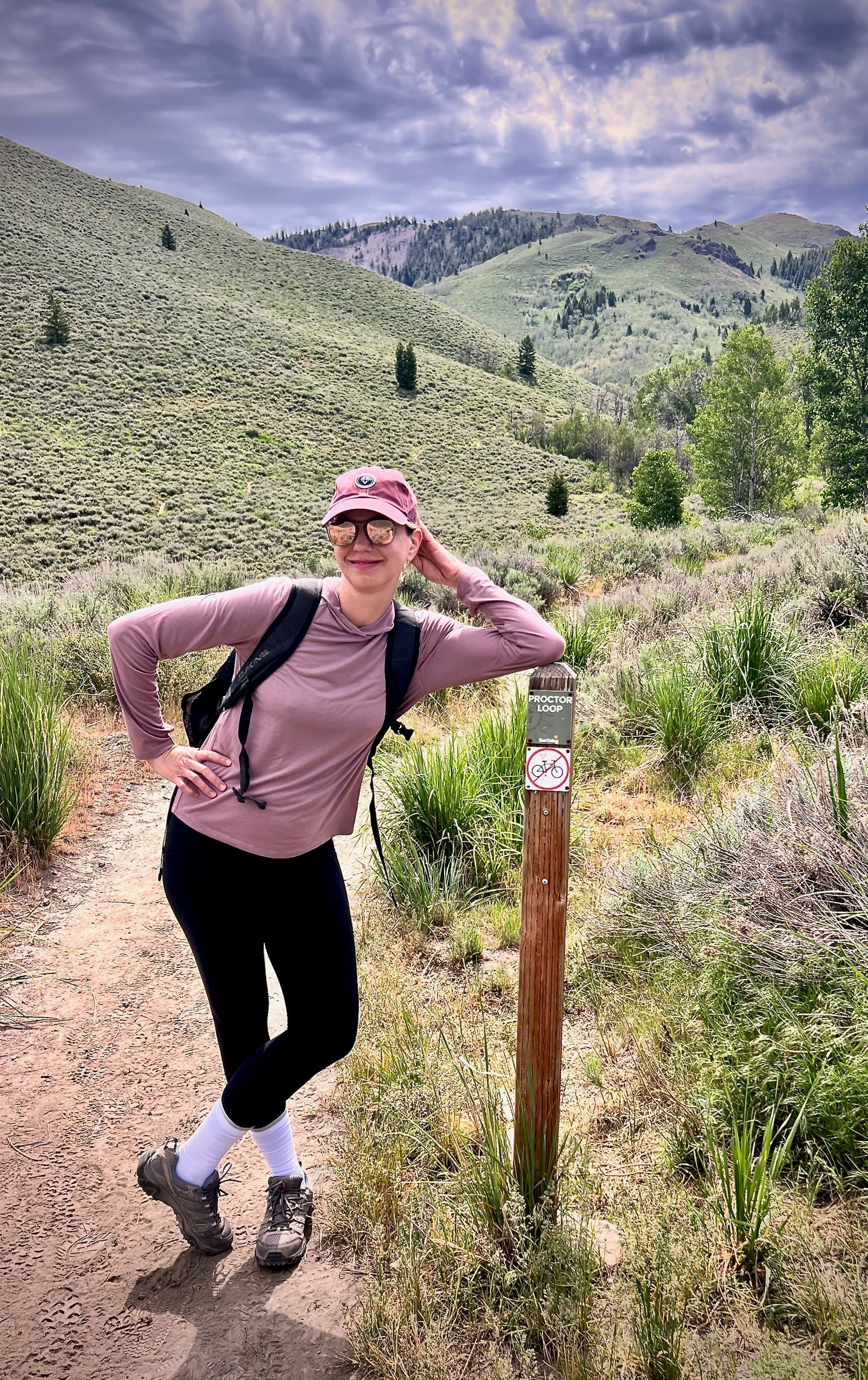 Sarah leaning on the sign post marker labeled "Proctor Loop" at the base of the trail.