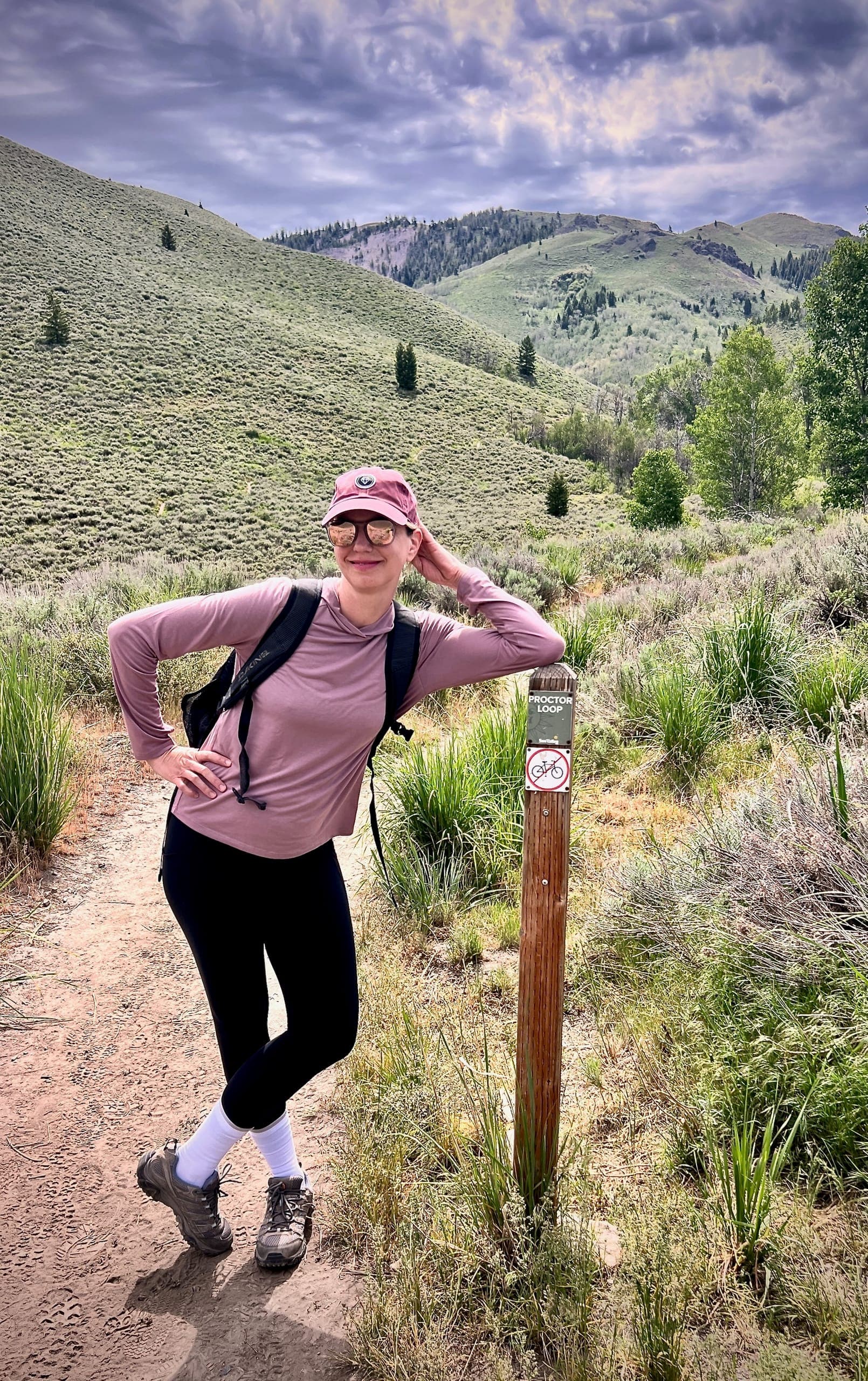 Sarah leaning on the sign post marker labeled "Proctor Loop" at the base of the trail.