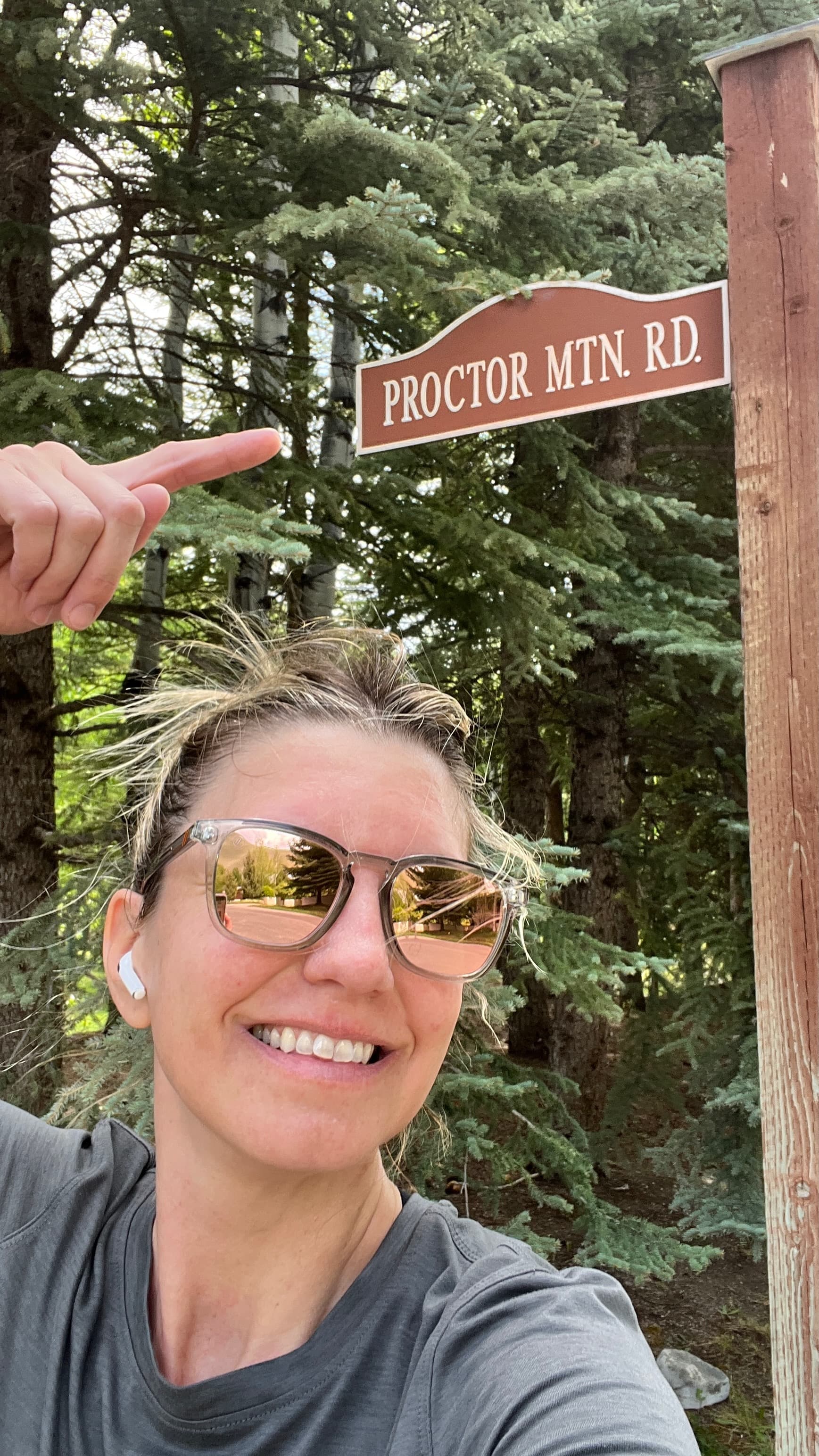 Selfie of Sarah pointing up at a brown "Proctor Mtn. Rd." sign.
