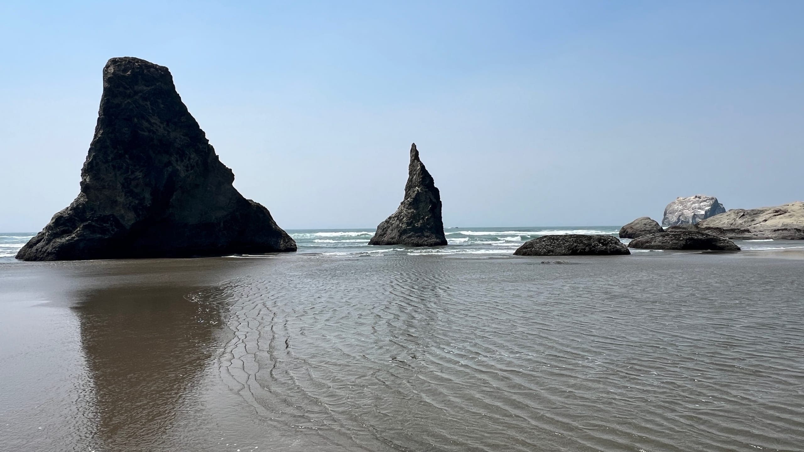 Pointy rock formations in the ocean viewed from a wide, sandy beach.